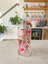 A 20oz glass beer can cup that has valentine designs around the cup in red, pink, yellow, and white. There is a heart shaped box of chocolates, champagne tower, bouquet of flowers, cherries, lockets, heart shaped cake, strawberries, bows, and flowers. The perfect galentine cup. 