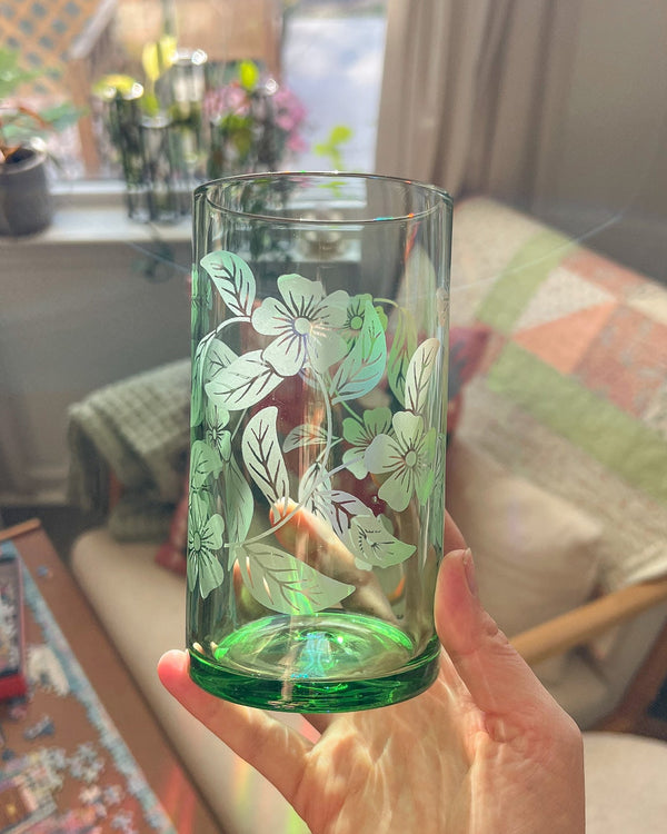 Hand holding a green glass with floral design indoors