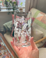 Hand holding a clear glass with floral etching in a home setting