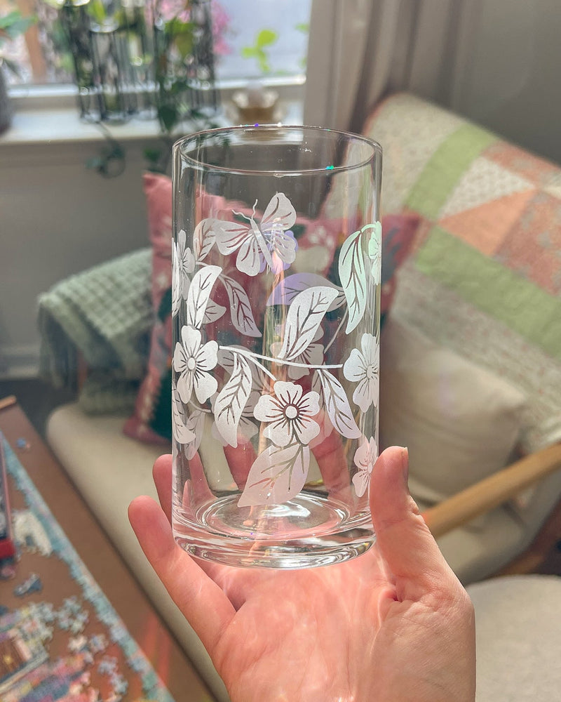 Hand holding a clear glass with floral etching in a home setting