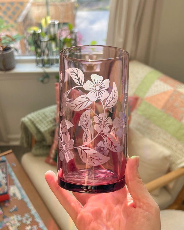 Hand holding a glass with floral etching in a home setting