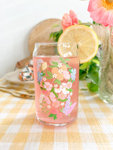 A cute 16oz glass coffee cup that is shaped like a beer can and has a butterfly garden design on the front with oranges, butterflies, pink and white flowers, and purple and blue flowers. 