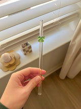 This is a glass straw that is bent at the top and has a green bow on it. 