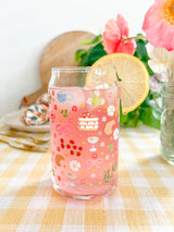 A cute 16oz glass coffee cup that is shaped like a beer can and has florals, bows, wine glass and rose bottle, tea cup, croissant, oranges, tomatoes, cake, espresso martini, pears and stars all around the glass in a repeating pattern. Color theme is pink, white, and green with a hint of blue and yellow. 