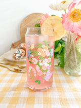 A cute 20oz glass coffee cup that is shaped like a beer can and has a butterfly garden design on the front with oranges, butterflies, pink and white flowers, and purple and blue flowers. 