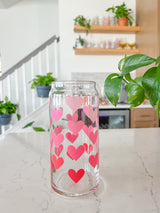 A cute libbey 20oz can glass coffee cup that is shaped like a beer can and has different shade of pink hearts around the glass. 