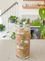 A cute 20oz libbey beer can glass coffee cup that is shaped like a beer can and has swans in water, lemons, oranges on branches, pink bows, and florals in a repeating pattern around the glass. 