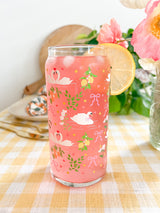 A cute 20oz libbey beer can glass coffee cup that is shaped like a beer can and has swans in water, lemons, oranges on branches, pink bows, and florals in a repeating pattern around the glass. 