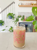 A cute 16oz glass coffee cup that is shaped like a beer can and has pink bows around the entire glass. Large pink bows are hot pink and small pink bows are light pink. 