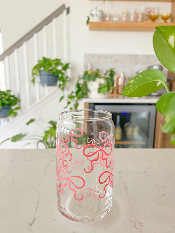 A cute 16oz glass coffee cup that is shaped like a beer can and has pink bows around the entire glass. Large pink bows are hot pink and small pink bows are light pink. 