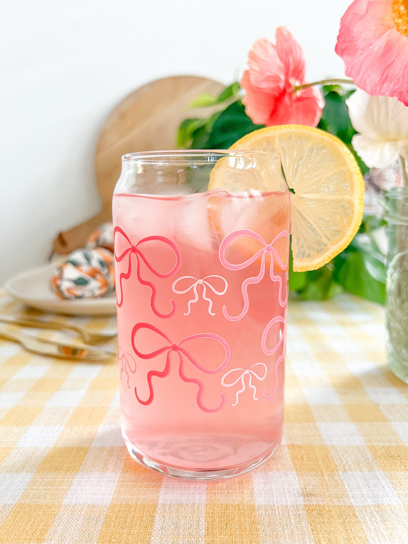 A cute 16oz glass coffee cup that is shaped like a beer can and has pink bows around the entire glass. Large pink bows are hot pink and small pink bows are light pink. 