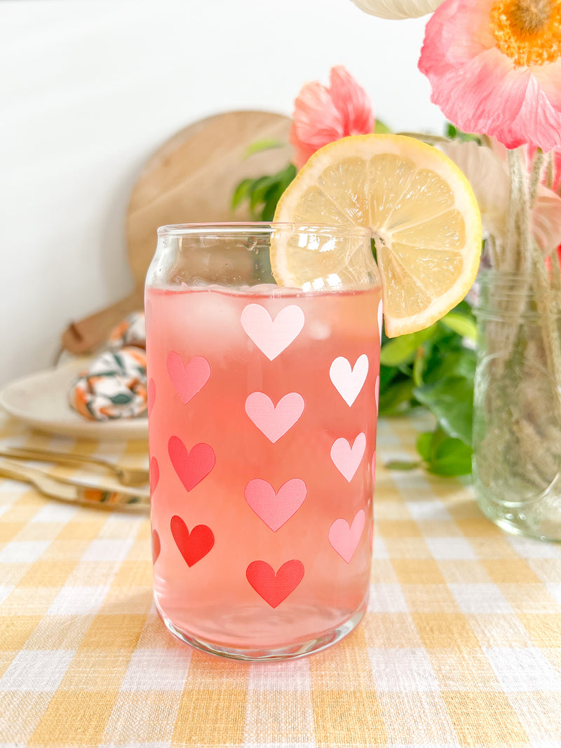 A cute 16oz glass coffee cup that is shaped like a beer can and has different shade of pink hearts around the glass. 