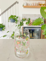 A cute 16oz glass coffee cup that is shaped like a beer can and has swans in water, lemons, oranges on branches, pink bows, and florals in a repeating pattern around the glass. 