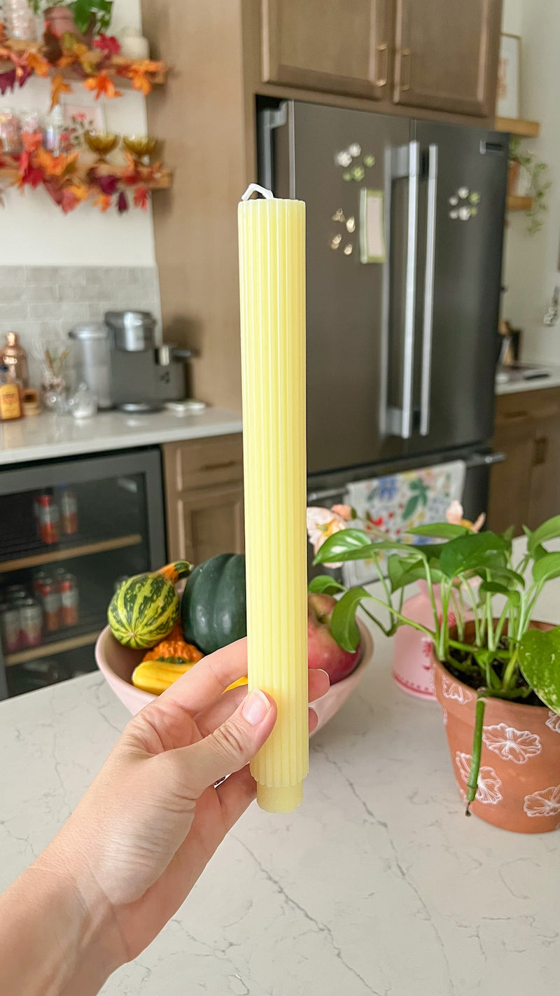 This is a taper candle that is yellow lemon in color and has a ribbed pattern on it. 