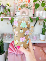 A cute 20oz glass coffee cup that is shaped like a beer can and has different colored candy hearts all over the glass with white daisies. Hearts are yellow, blue, pink, green, and orange and say cute drinks inside the heart.