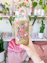 A cute 20oz libbey beer can glass coffee cup that is shaped like a beer can and has a design on the front of the glass that say "XO OX XO" and has florals and butterflies with heart wings around the letters. The colors are hot pink, light pink and pops of yellow and white. 