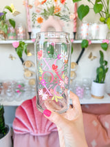 A cute 20oz libbey beer can glass coffee cup that is shaped like a beer can and has a design on the front of the glass that say "XO OX XO" and has florals and butterflies with heart wings around the letters. The colors are hot pink, light pink and pops of yellow and white. 