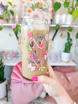 A cute 20oz libbey beer can glass coffee cup that is shaped like a beer can and has a design on the front of the glass that say "XO OX XO" and has florals and butterflies with heart wings around the letters. The colors are hot pink, light pink and pops of yellow and white. 